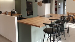A modern kitchen with a central island, bar stools, and a dining area with a wooden table and chairs. - Sunny vacation home. Ideally located between lake, beach and forest. (Sanguinet)