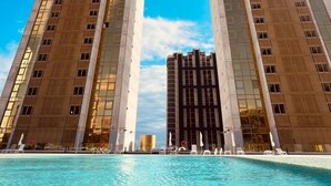 Um hotel alto com um átrio central e uma área de piscina à frente.