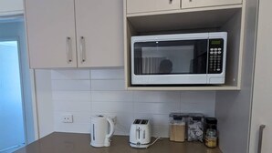 A kitchenette with a microwave, toaster, kettle, and a small cabinet with jars.