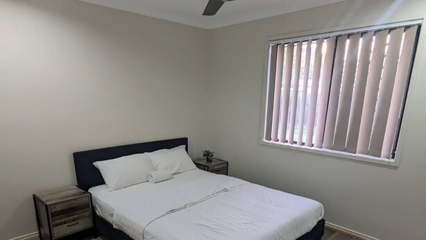 A bedroom with a bed, a nightstand, a ceiling fan, and a window with blinds.