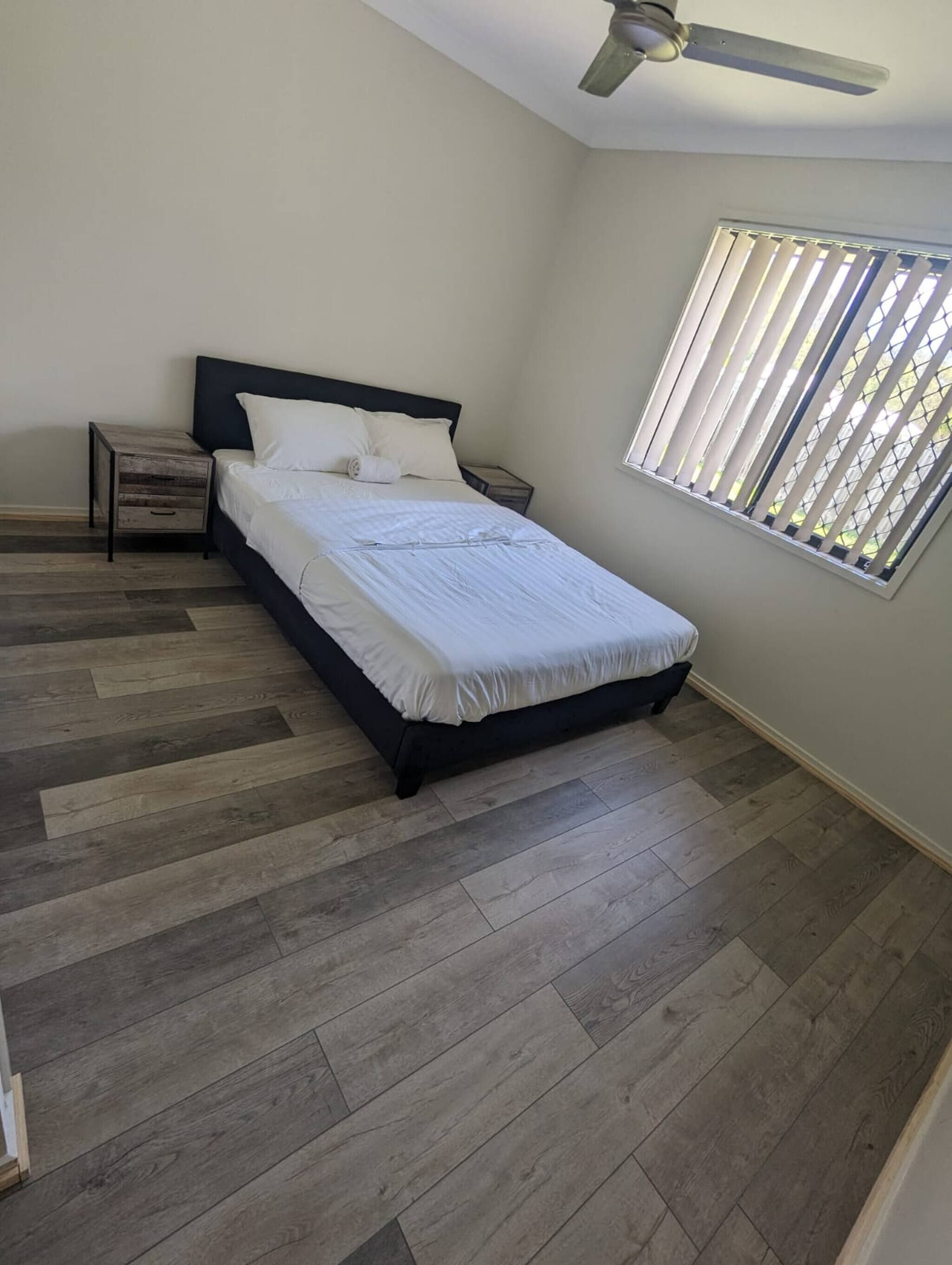 A bedroom with a bed, a nightstand, a ceiling fan, and a window with blinds.