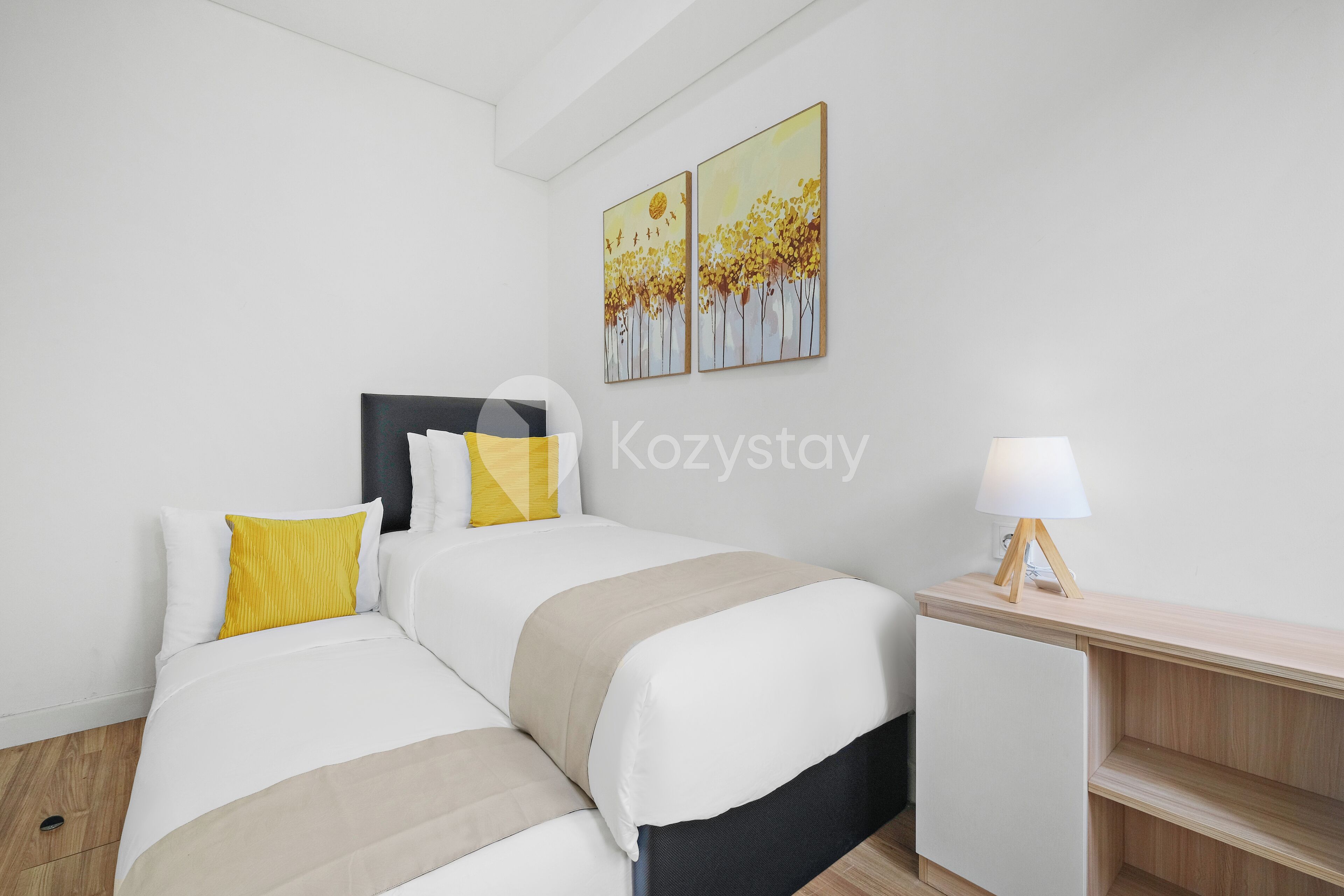 A modern bedroom with two beds, a bedside table, and a lamp.