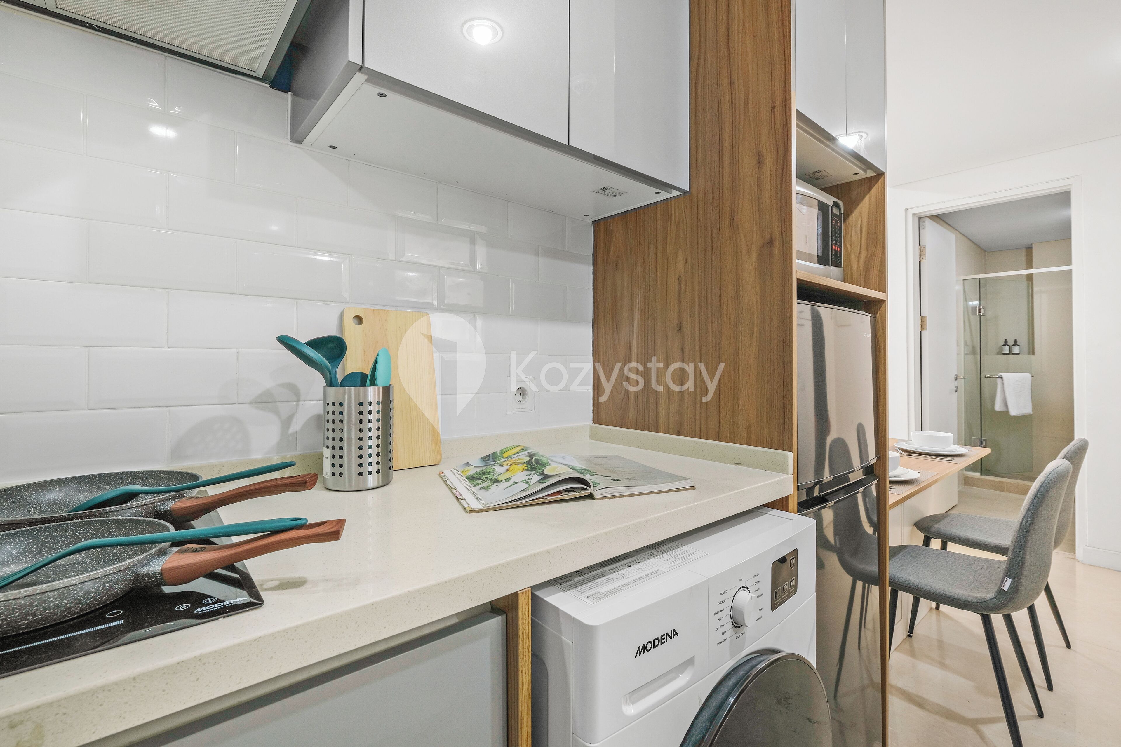 A modern kitchen with white tiles, a washing machine, a dining area with a table and chairs, and a wooden cabinet.