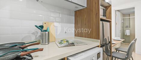 A modern kitchen with white tiles, a washing machine, a dining area with a table and chairs, and a wooden cabinet.