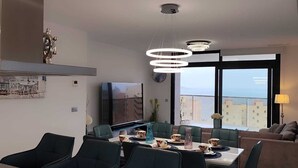 A modern kitchen with a dining area, a large window with a city view, and a living area with a sofa and lamp. - Sunset Cliffs Residence (Benidorm)