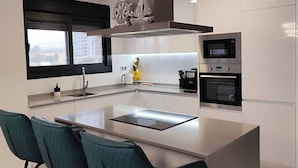 A modern kitchen with a central island, bar stools, built-in appliances, and a view through a window. - Sunset Cliffs Residence (Benidorm)