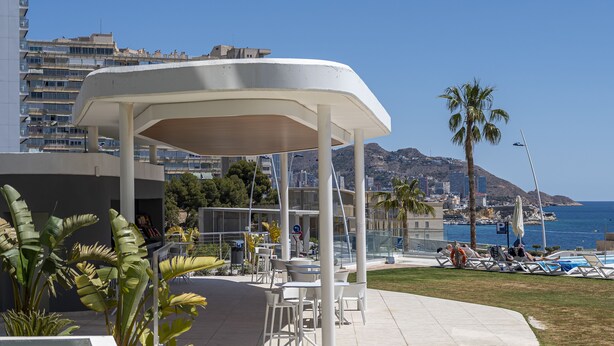 A covered outdoor seating area with tables and chairs, overlooking a pool and a coastal view. - Sunset Cliffs Residence (Benidorm)