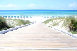 A wooden boardwalk leading to a beach with blue umbrellas and white lounge chairs. - Salty Rose Inn by AvantStay | Inlet Beach Home w/ Porch, Firepit & Pool Access (Inlet Beach)