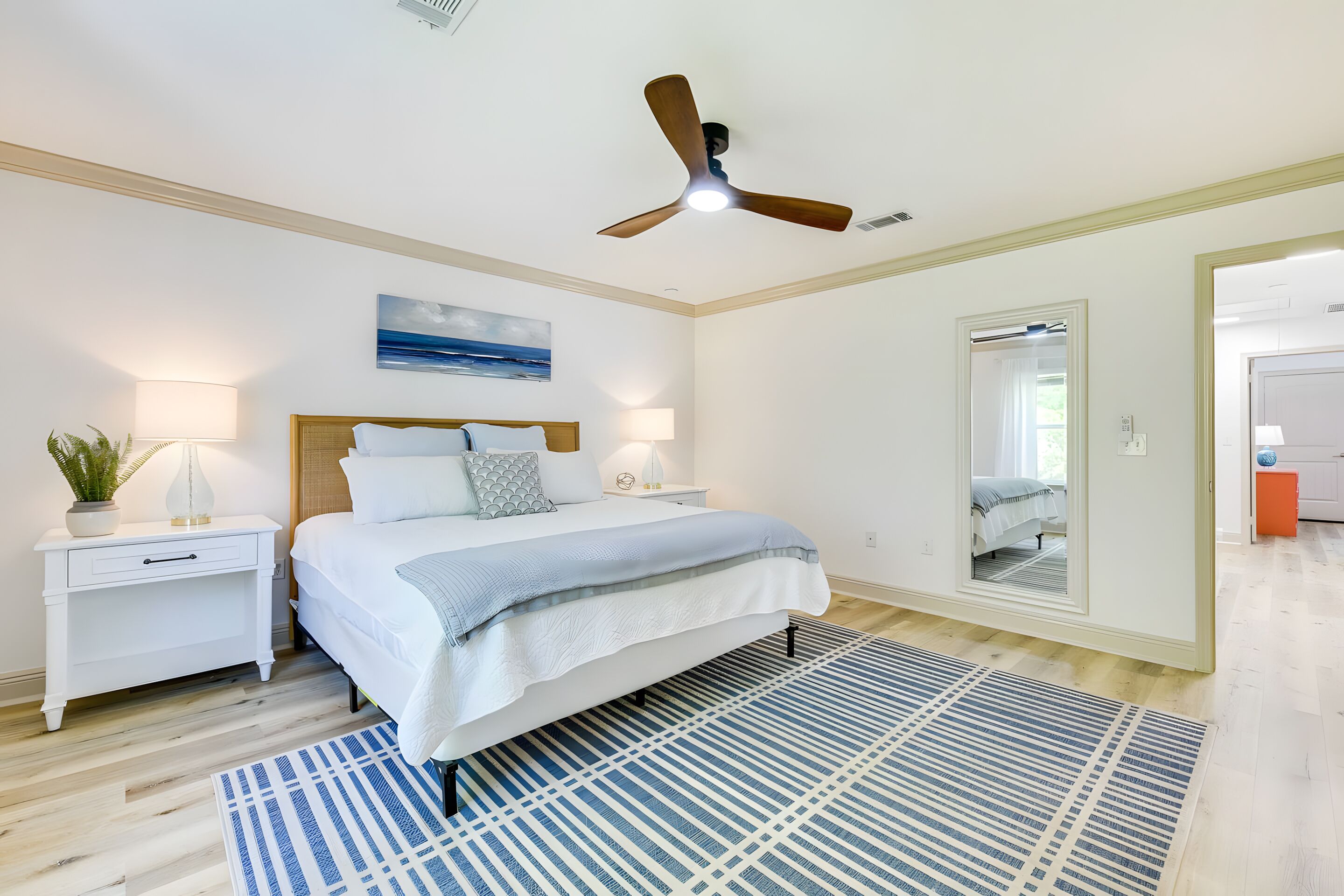 A bedroom with a bed, nightstands, a ceiling fan, a large mirror, and a view into another room.