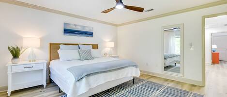 A bedroom with a bed, nightstands, a ceiling fan, a large mirror, and a view into another room.