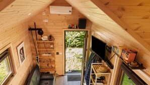 Una cabaña acogedora con cama altillo, un banco de madera, una mesita y una puerta que da a un espacio exterior.