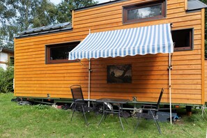 Une maison mobile dotée d’un auvent à rayures, d’une table à manger, de chaises et d’un tableau accroché au mur.