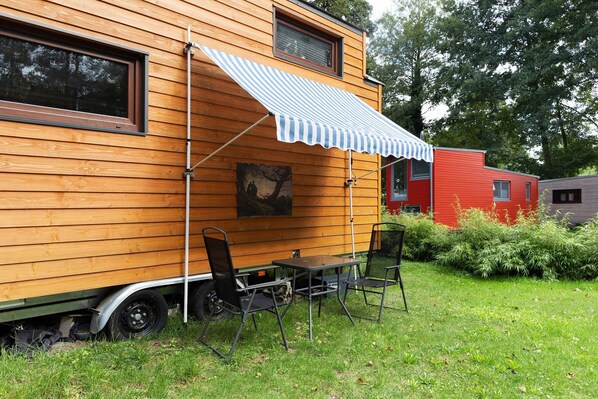 Une maison en bois avec un auvent rayé, une table avec des chaises et un tableau accroché au mur.