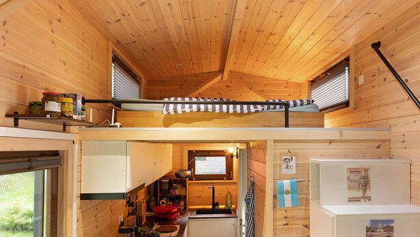 Una cabaña de madera compacta con habitación en altillo, kitchenette y baño pequeño.