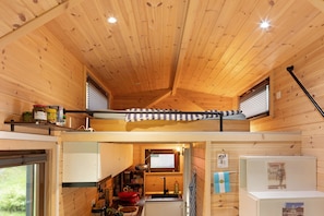Une petite cabane en bois avec une chambre à coucher en mezzanine, une kitchenette et une petite salle de bain.