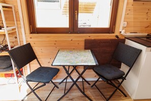 Une petite pièce en bois, avec une table et deux chaises, une fenêtre et une étagère où sont posés divers objets.