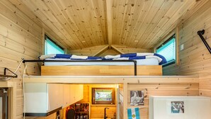 Une cabane en bois avec un lit superposé, un petit coin cuisine et une fenêtre avec des stores.