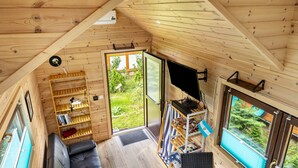Un intérieur en bois avec un canapé, des étagères, une table et une vue sur la verdure à l’extérieur.