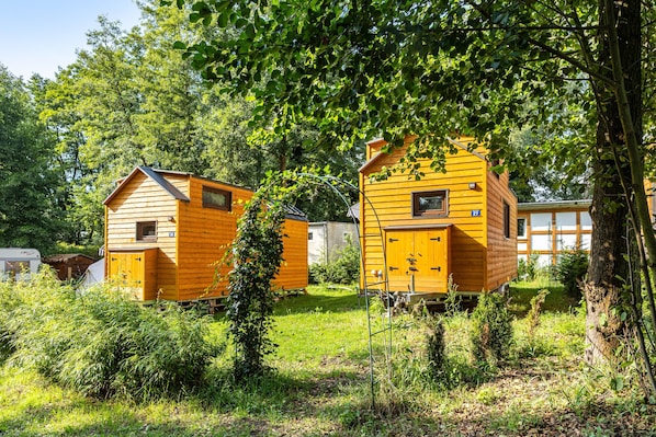 Two wooden cabins with a small window and door, surrounded by greenery and trees.