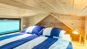 Une chambre avec un plafond en bois, un lit avec une literie bleue et blanche, une fenêtre avec des stores et une lampe de chevet.