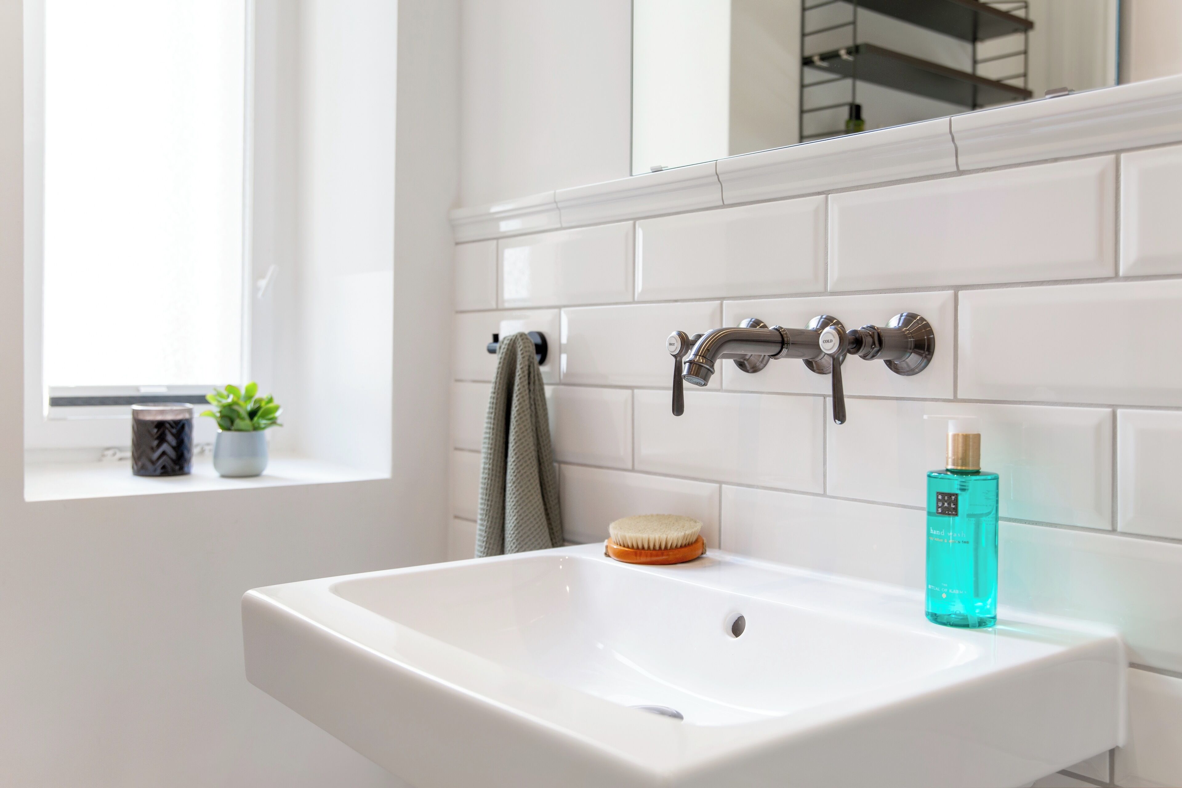 A bathroom with a white sink, a mirror, and a window.