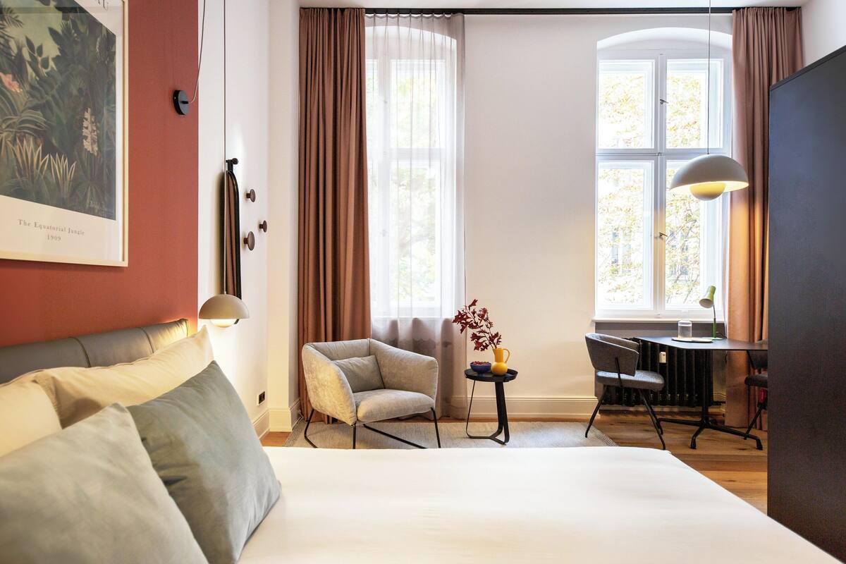 Ein Hotelzimmer mit Bett, Stuhl, Schreibtisch und einem Fenster mit Vorhängen.