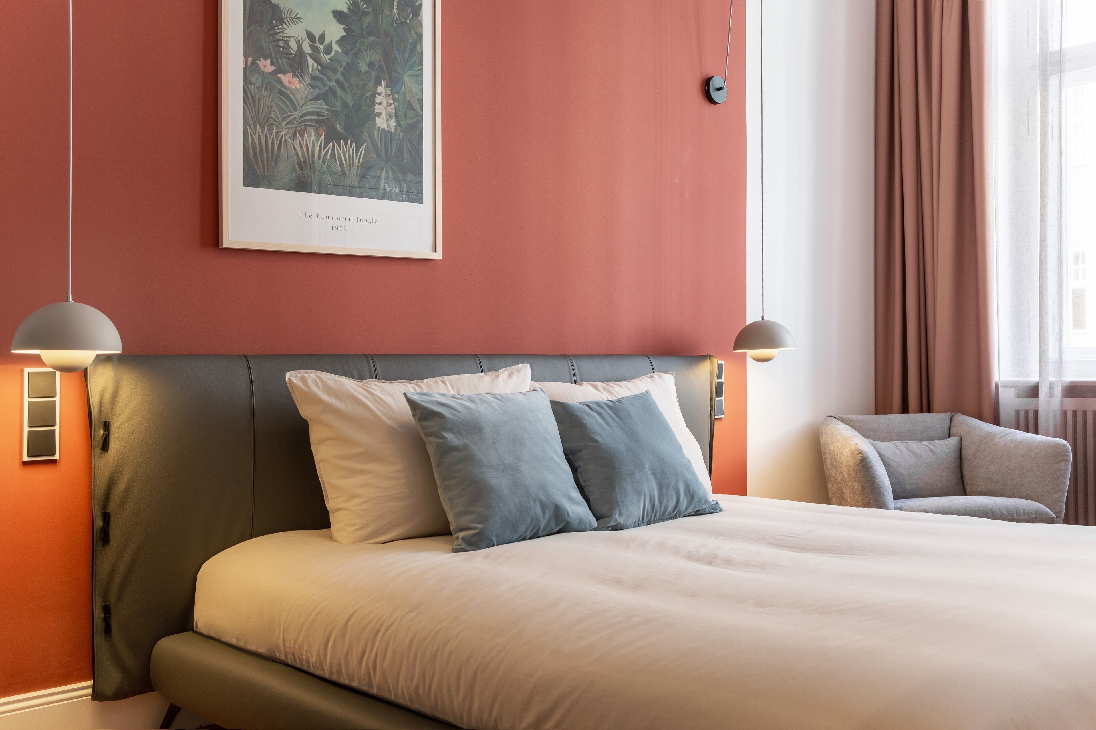Une chambre d’hôtel avec un grand lit, deux lampes de chevet, un tableau encadré au mur et une fenêtre avec des rideaux.
