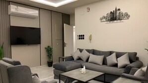 A modern living room with a grey sofa, a coffee table, and a TV mounted on the wall. - Downtown Suites Orbitnet (Madinah)