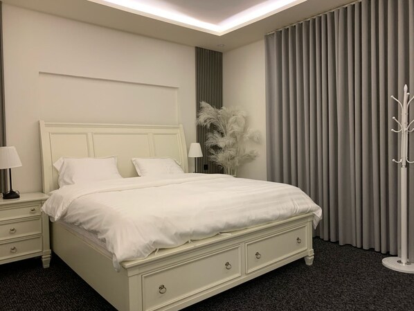 A neatly arranged bedroom with a large bed, bedside tables, a lamp, and a decorative plant.