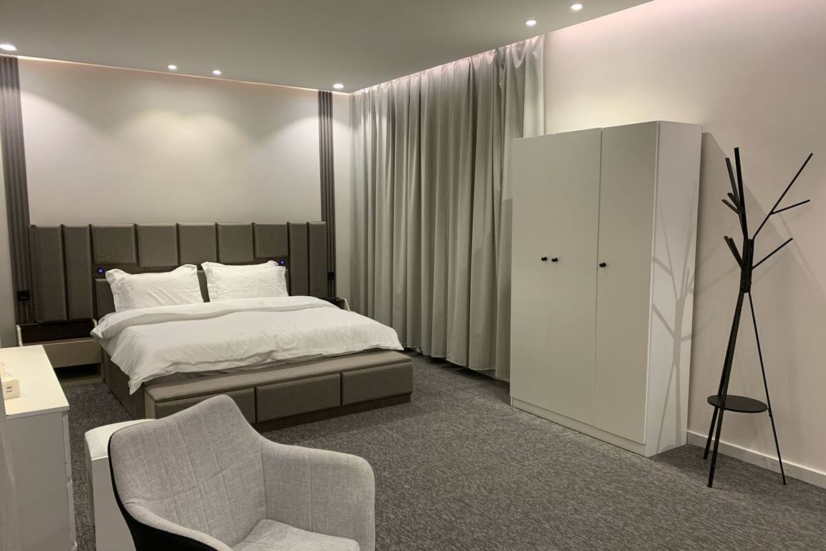 A modern hotel room with a bed, a wardrobe, a chair, and a floor lamp.