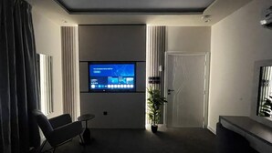 A modern living room with a flat-screen TV mounted on the wall, a seating area with a sofa and a small table, and a potted plant. - Downtown Suites Orbitnet (Madinah)