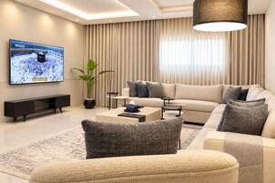 A modern living room with a flat-screen TV, a sofa set, a coffee table, and a potted plant.
