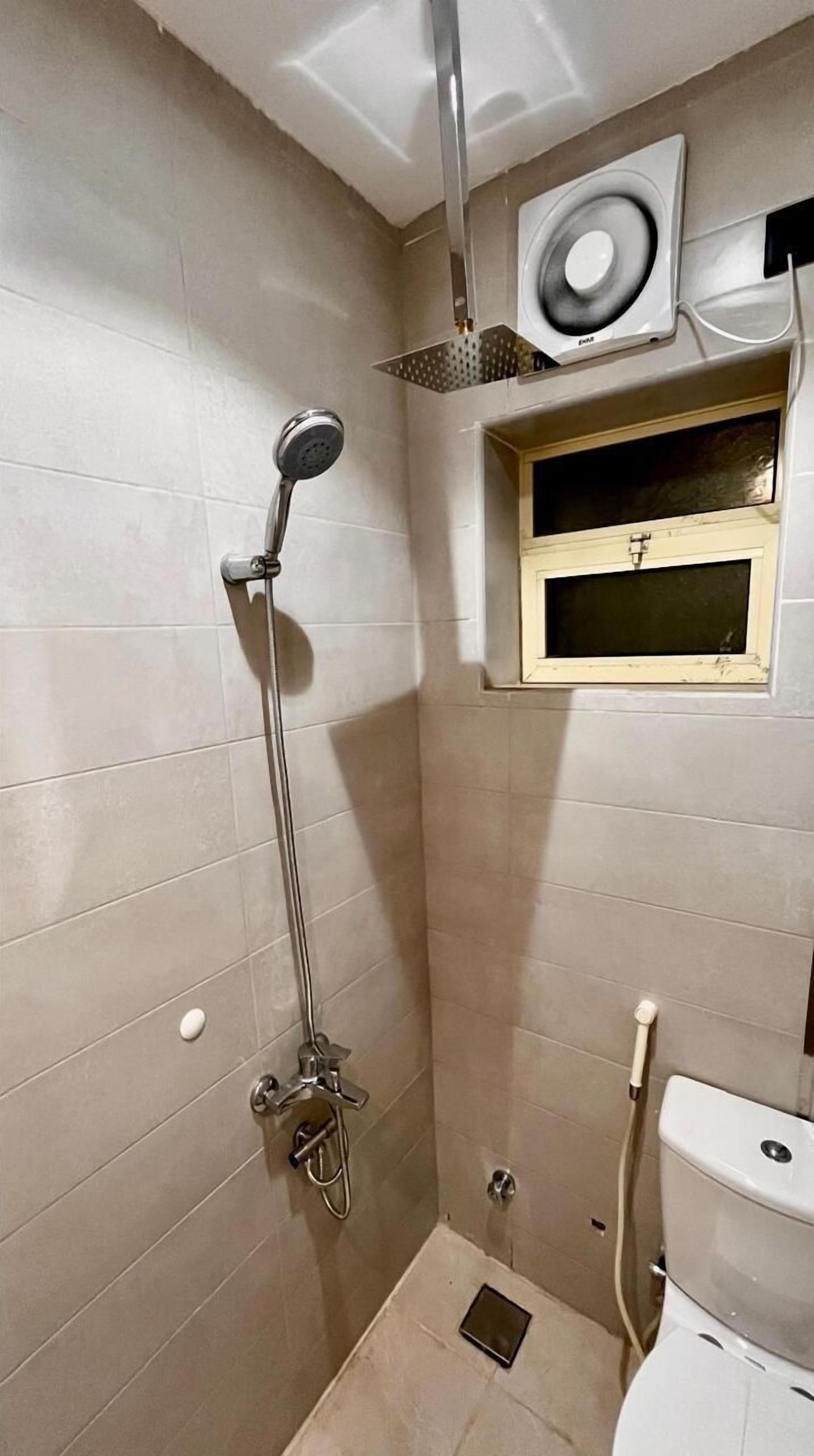 A small bathroom with a shower, toilet, and a window above the toilet.