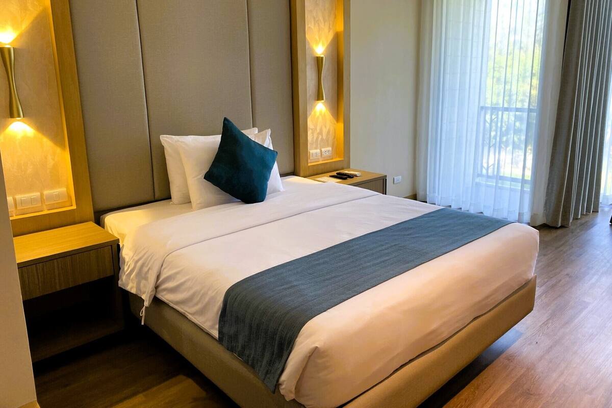 A hotel room with a large bed, two bedside tables, a nightstand, and a window with curtains.