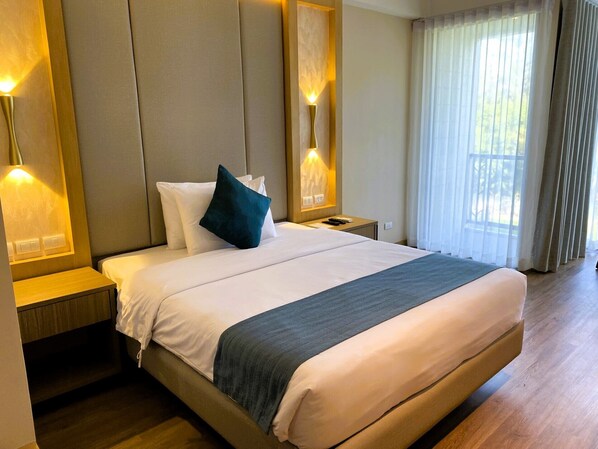 Una habitación de hotel con una cama grande, dos mesitas de noche y un ventanal con cortinas.