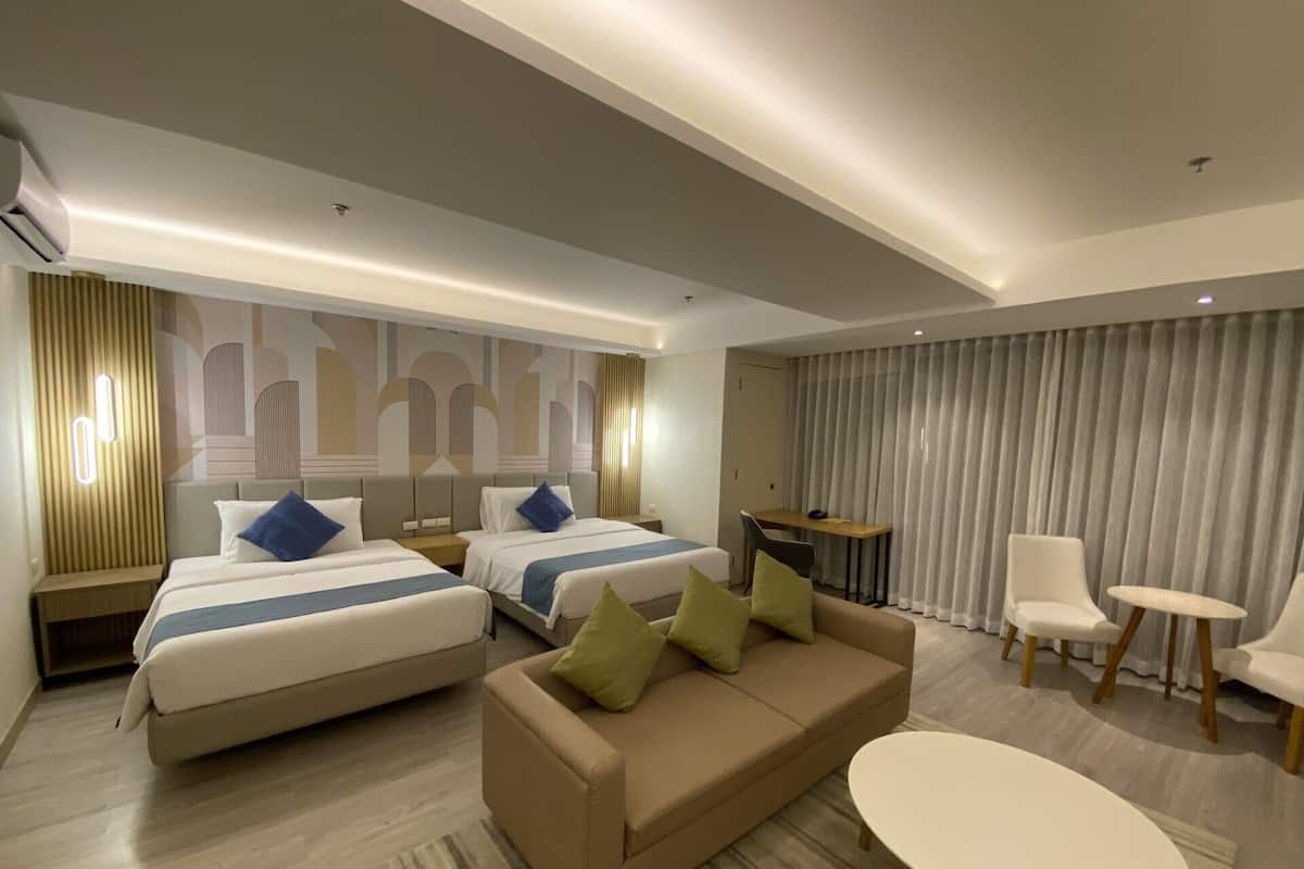 A modern hotel room with two beds, a sofa, a small table, and a chair.