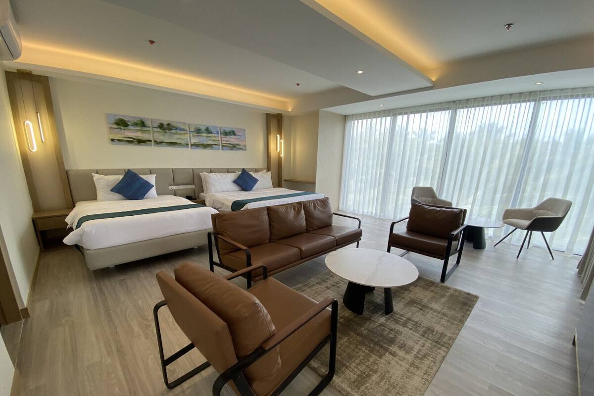 A modern hotel room with a large bed, two sofas, a coffee table, and a seating area with chairs.