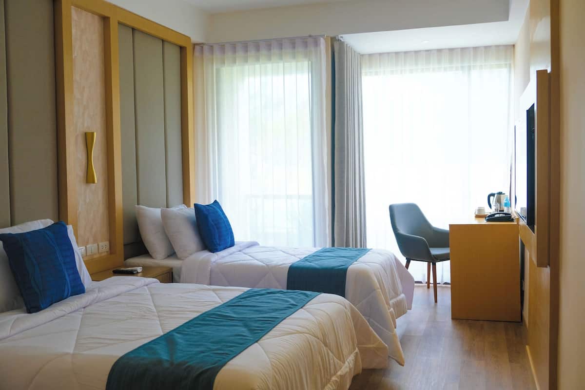 A hotel room with two beds, a desk, a chair, and a television.