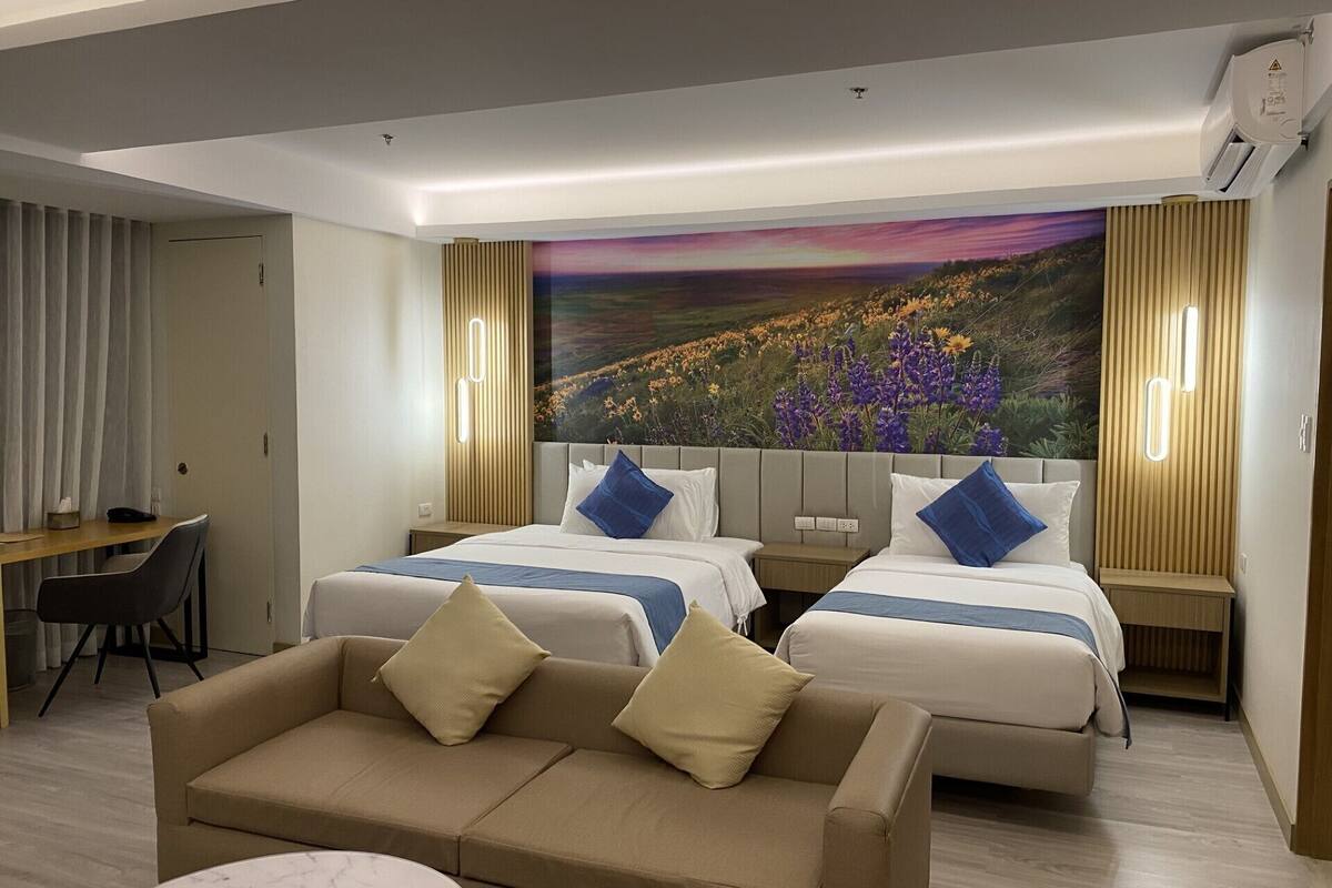 A hotel room with two beds, a sofa, a desk, and a large painting on the wall.