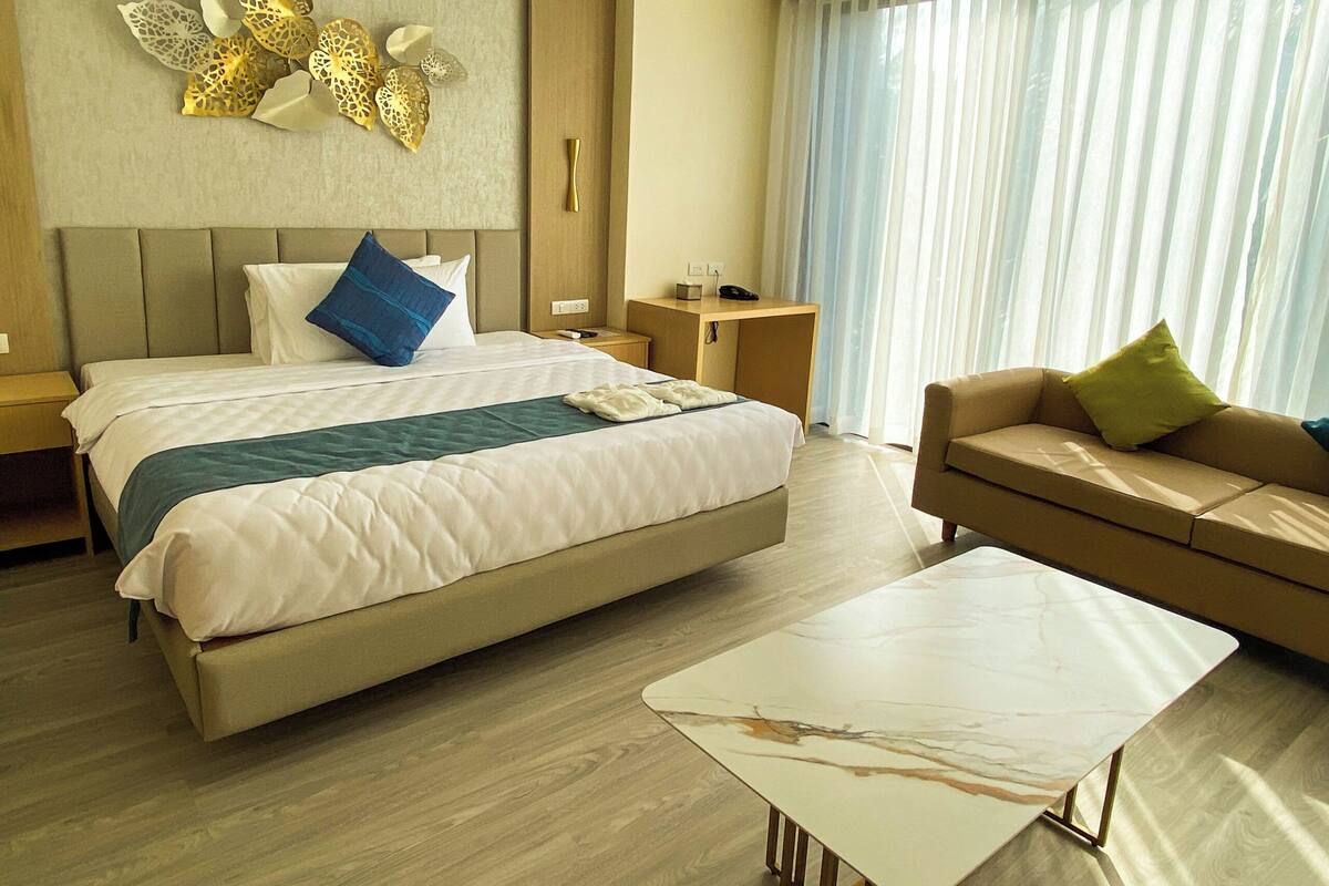 A hotel room with a bed, a sofa, a coffee table, a desk, and a wall with decorative elements.
