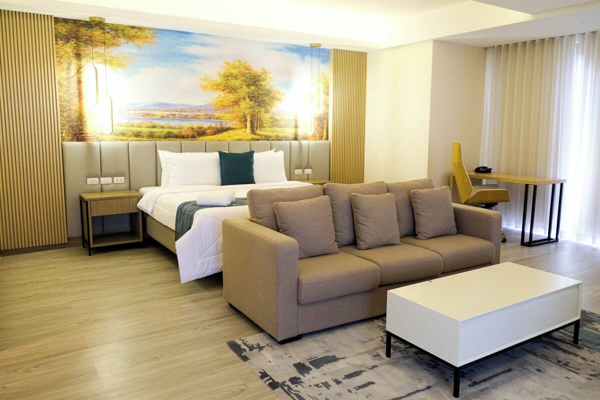 A modern hotel room with a bed, sofa, and a small table.