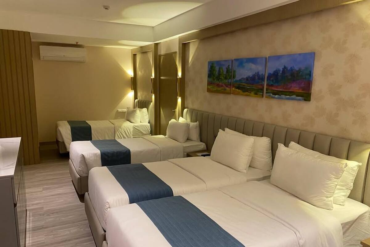 A hotel room with three beds, a desk, and a painting on the wall.