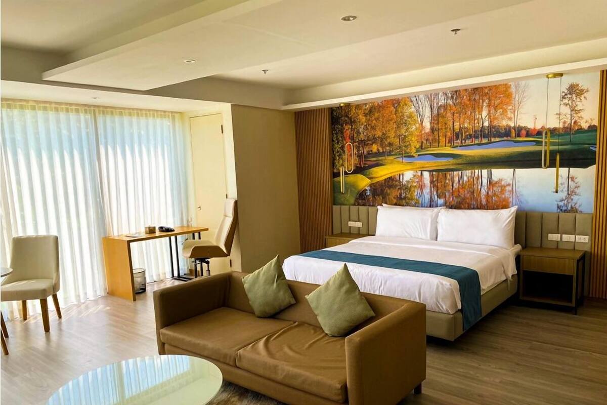 A hotel room with a bed, a sofa, a desk, and a painting of a landscape.