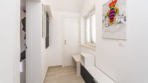 Een gang met een witte deur, een bank en een aan de muur hangend kunstwerk.