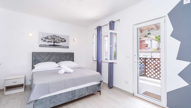 Een slaapkamer met een bed, nachtkastje, raam met gordijnen, en een deur naar een buitenruimte.