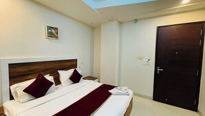 Een hotelkamer met een groot bed, een houten hoofdeinde, een rode plaid, een nachtkastje, een wandlamp en een deur.
