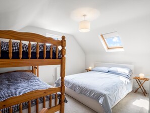A bedroom with a bunk bed, a single bed, a bedside table with a lamp, and a skylight.