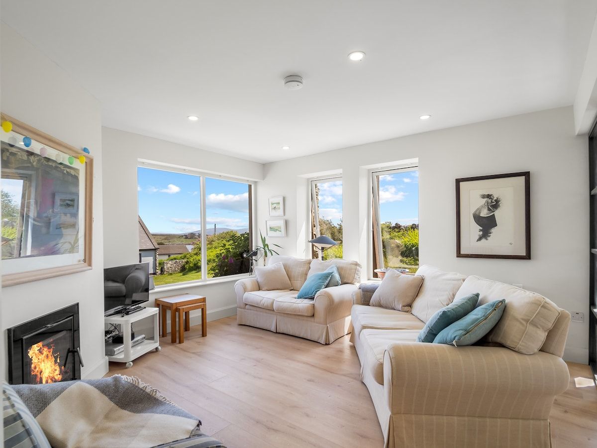 A spacious living room with a fireplace, large windows, and a view of the outdoors.