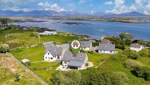 A coastal property with a house, a fenced yard, and a view of the sea and mountains.
