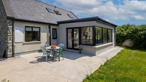 A modern house with a stone exterior, a covered patio with a table and chairs, and a large glass window.